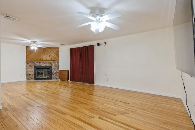 unfurnished living room featuring visible vents, light wood-style flooring, a glass covered fireplace, ceiling fan, and baseboards