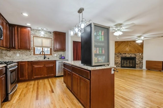 kitchen with light wood finished floors, appliances with stainless steel finishes, a sink, and a stone fireplace