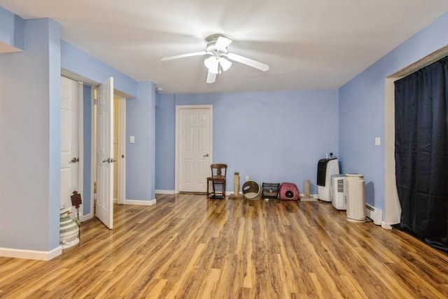 interior space featuring a ceiling fan, light wood-style flooring, a baseboard heating unit, and baseboards