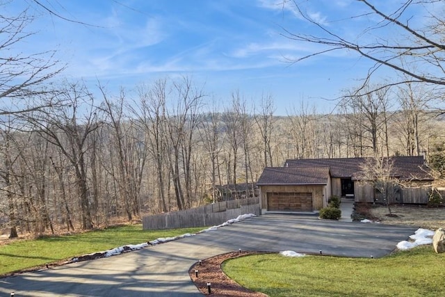 view of front facade featuring driveway, a forest view, an attached garage, fence, and a front yard