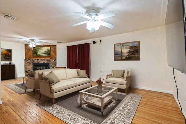 living room with ceiling fan, a fireplace, visible vents, baseboards, and light wood finished floors