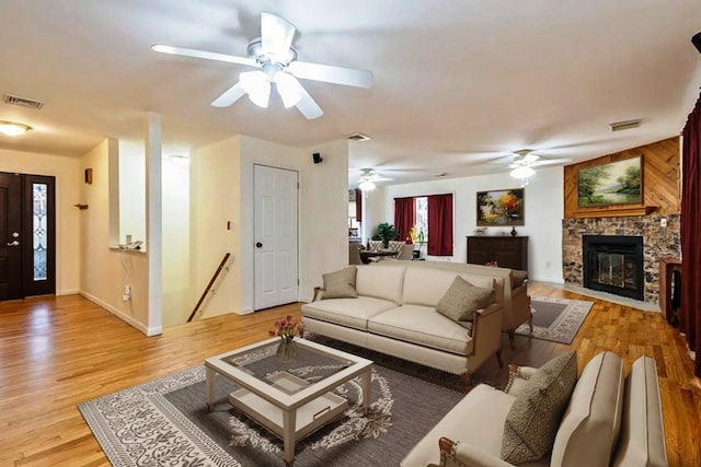 living room featuring light wood-style floors, ceiling fan, visible vents, and a stone fireplace