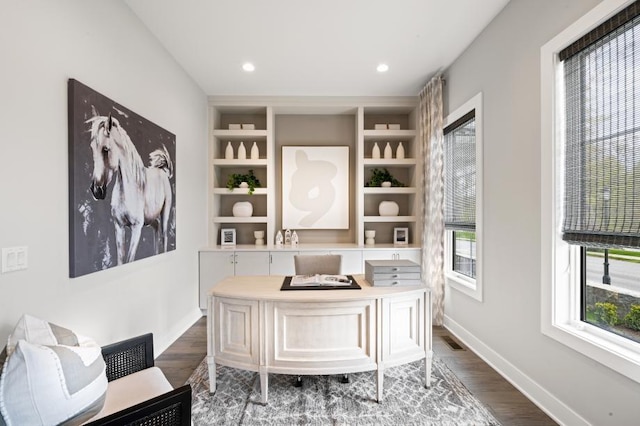 home office with built in shelves and dark hardwood / wood-style flooring