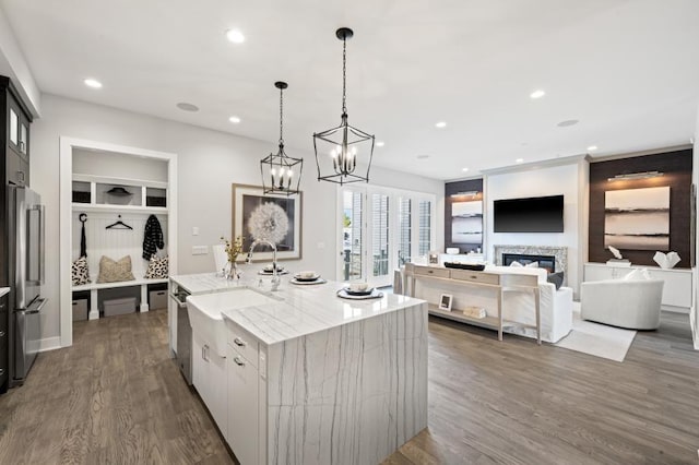 kitchen with stainless steel refrigerator, hanging light fixtures, light stone counters, dark hardwood / wood-style floors, and a center island with sink