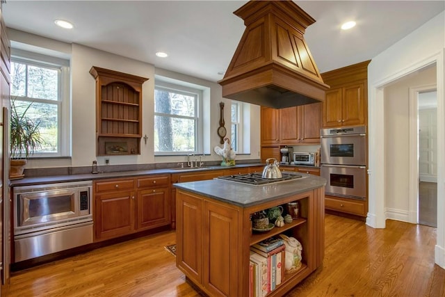 kitchen with sink, stainless steel appliances, a kitchen island, custom range hood, and light wood-type flooring