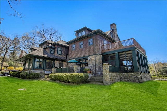 rear view of house with a sunroom, a balcony, and a lawn