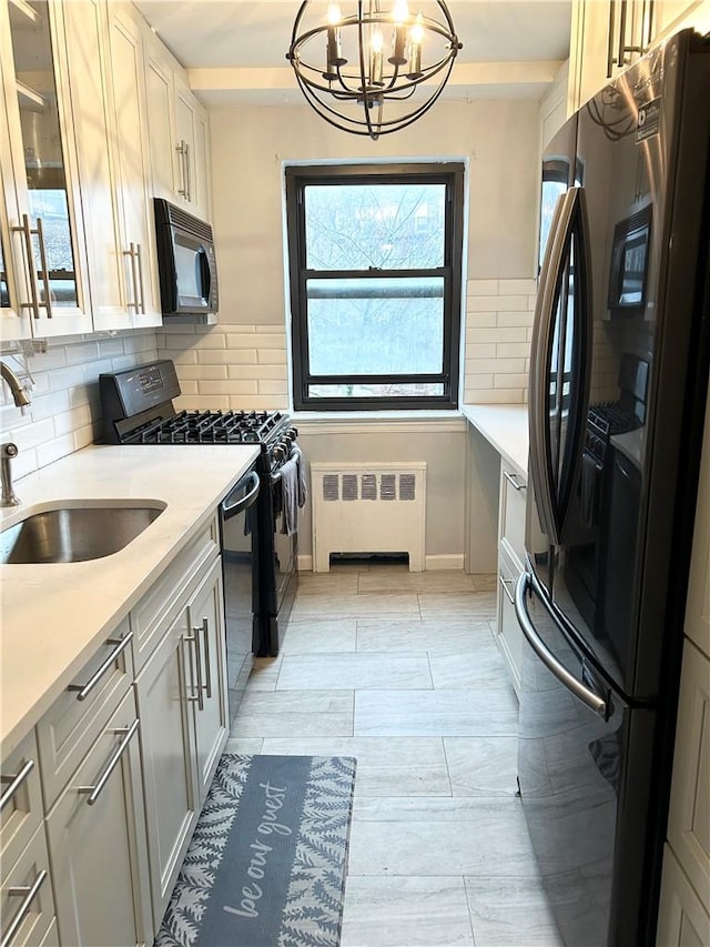 kitchen featuring pendant lighting, black appliances, sink, decorative backsplash, and radiator heating unit