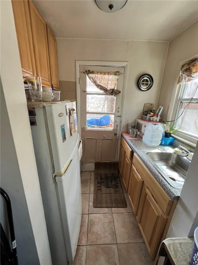 kitchen with white refrigerator, light tile patterned flooring, and sink