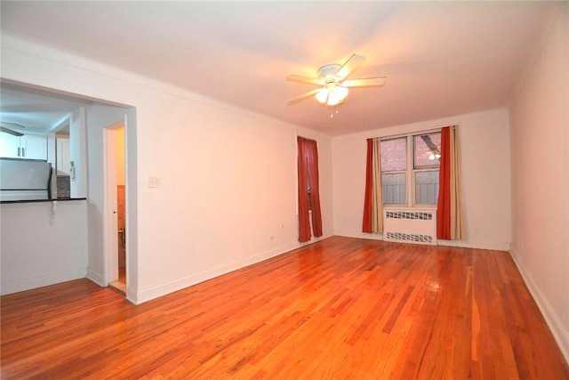 unfurnished room with radiator heating unit, light wood-type flooring, and ceiling fan