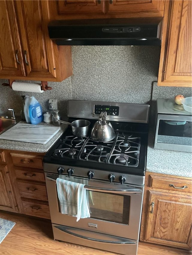 kitchen featuring range hood, backsplash, appliances with stainless steel finishes, and light hardwood / wood-style flooring