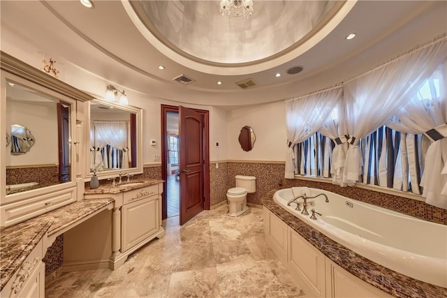 bathroom with a washtub, a raised ceiling, toilet, vanity, and tile walls