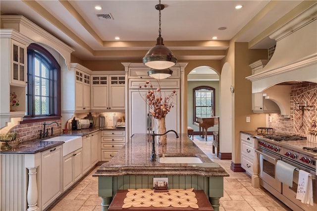 kitchen with pendant lighting, sink, high end appliances, and an island with sink