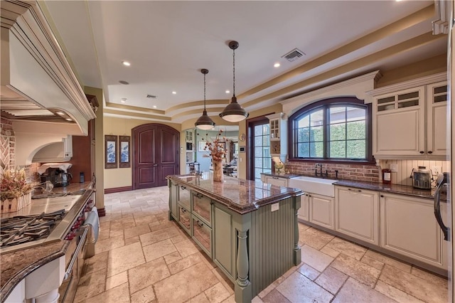 kitchen with dark stone counters, a raised ceiling, sink, hanging light fixtures, and a kitchen island