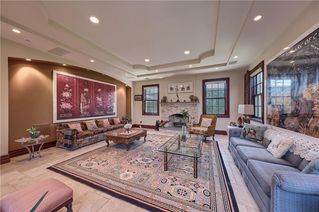 living room with a raised ceiling and a stone fireplace