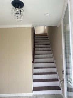 stairs with crown molding and a notable chandelier