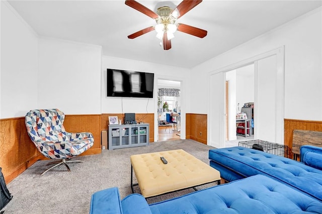 carpeted living room featuring ceiling fan, wood walls, and crown molding