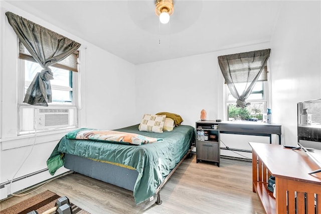 bedroom with light hardwood / wood-style floors, a baseboard radiator, ceiling fan, and cooling unit