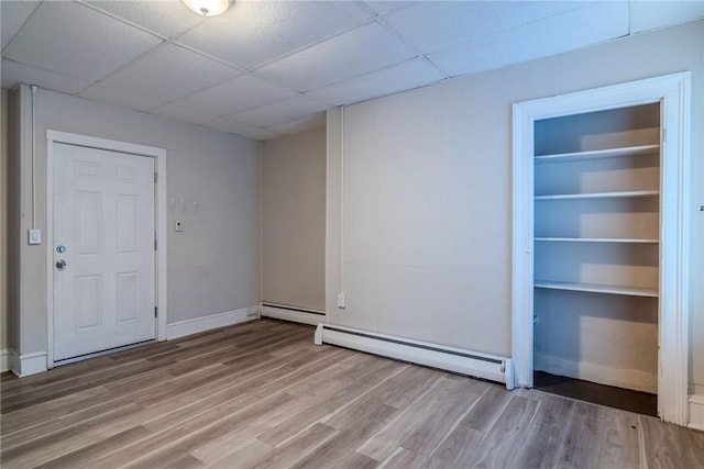 empty room featuring a paneled ceiling, hardwood / wood-style floors, and a baseboard heating unit