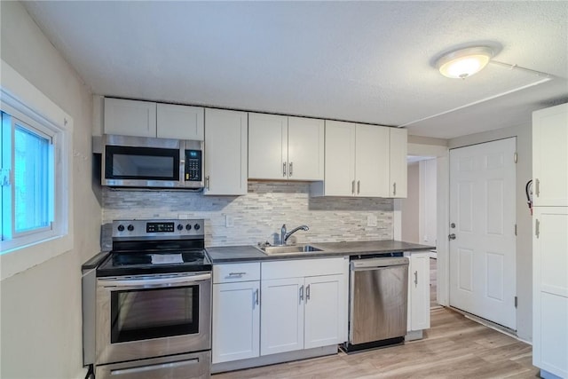 kitchen with appliances with stainless steel finishes, light wood-type flooring, tasteful backsplash, sink, and white cabinetry