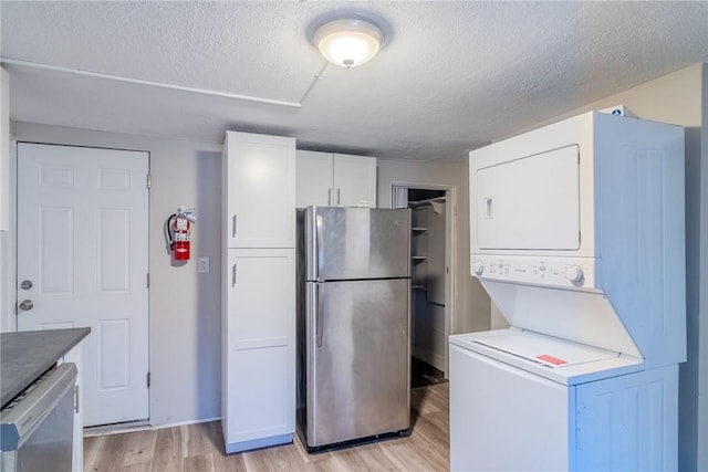 kitchen with white cabinetry, stacked washer / dryer, a textured ceiling, appliances with stainless steel finishes, and light wood-type flooring