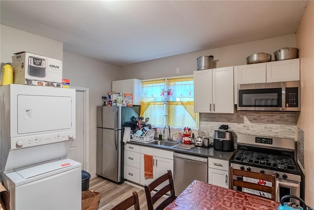 kitchen featuring stainless steel appliances, white cabinetry, stacked washer / dryer, and sink