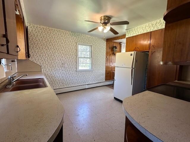 kitchen featuring ceiling fan, sink, a baseboard heating unit, and white refrigerator