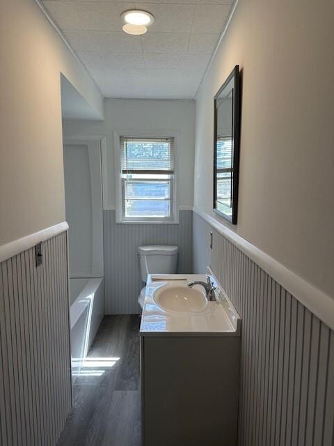 bathroom with hardwood / wood-style floors, vanity, toilet, and a tub to relax in