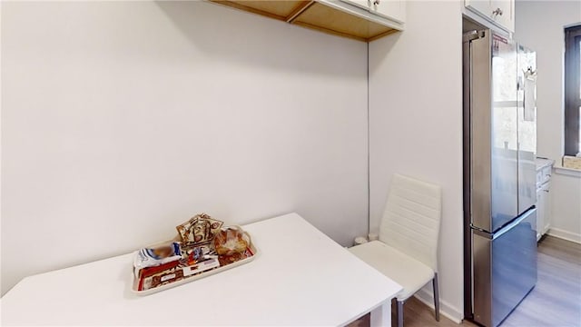 interior space with stainless steel fridge, white cabinets, and wood-type flooring