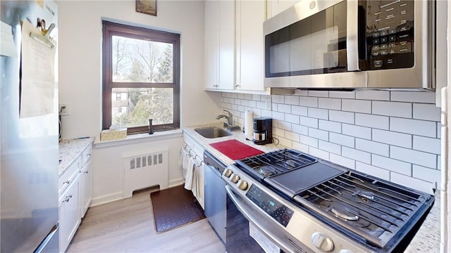 kitchen featuring appliances with stainless steel finishes, radiator, sink, light hardwood / wood-style flooring, and white cabinets