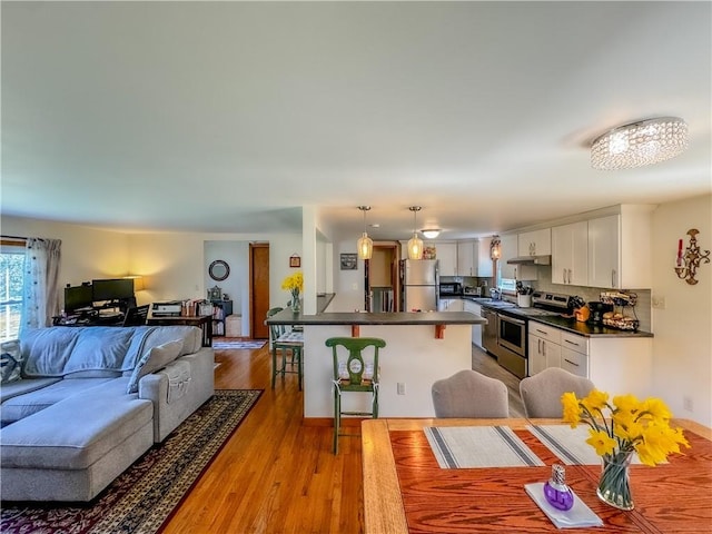 interior space featuring white cabinets, hanging light fixtures, a breakfast bar area, light hardwood / wood-style floors, and stainless steel appliances