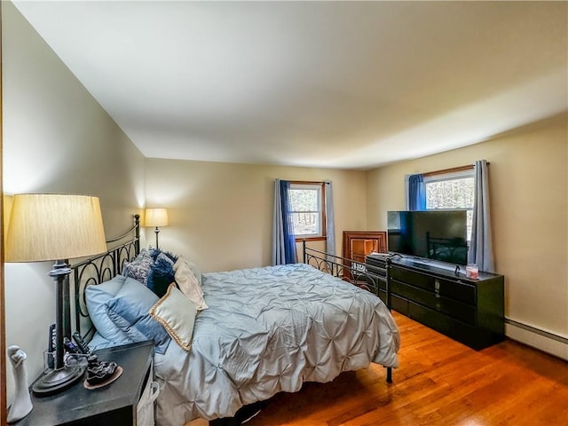 bedroom featuring multiple windows, wood-type flooring, and a baseboard heating unit