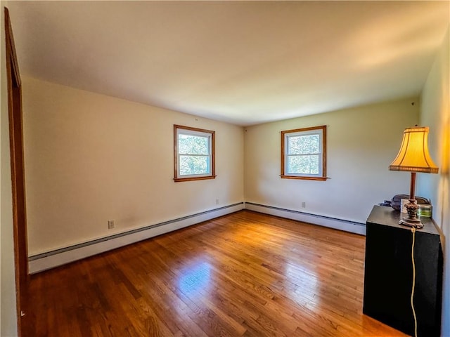 spare room with baseboard heating, a healthy amount of sunlight, and hardwood / wood-style flooring