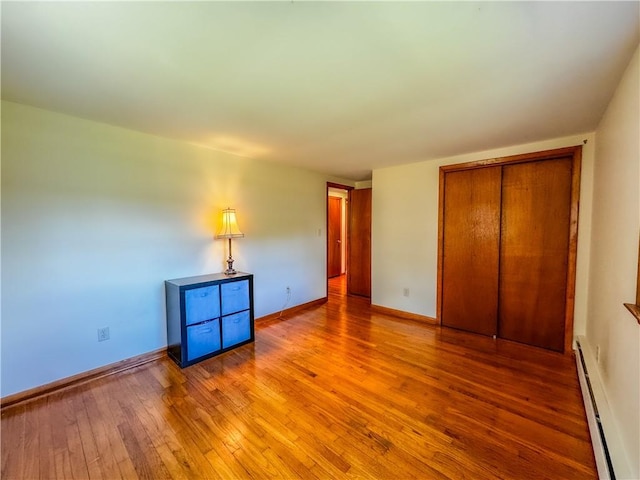 unfurnished bedroom featuring hardwood / wood-style flooring, a closet, and a baseboard heating unit