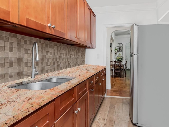 kitchen with stainless steel fridge, light stone counters, crown molding, sink, and light hardwood / wood-style flooring