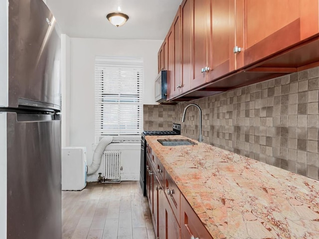 kitchen featuring light stone countertops, appliances with stainless steel finishes, tasteful backsplash, light hardwood / wood-style floors, and radiator heating unit