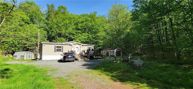 27 Birch Ln, Livingston Manor, NY 12768 - view of front of house with a storage unit, a wooden deck, gravel driveway, and a view of trees