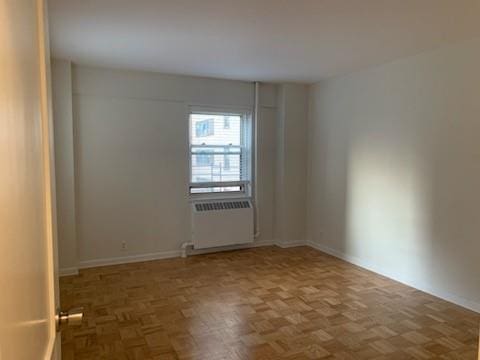 empty room featuring dark parquet floors and radiator heating unit