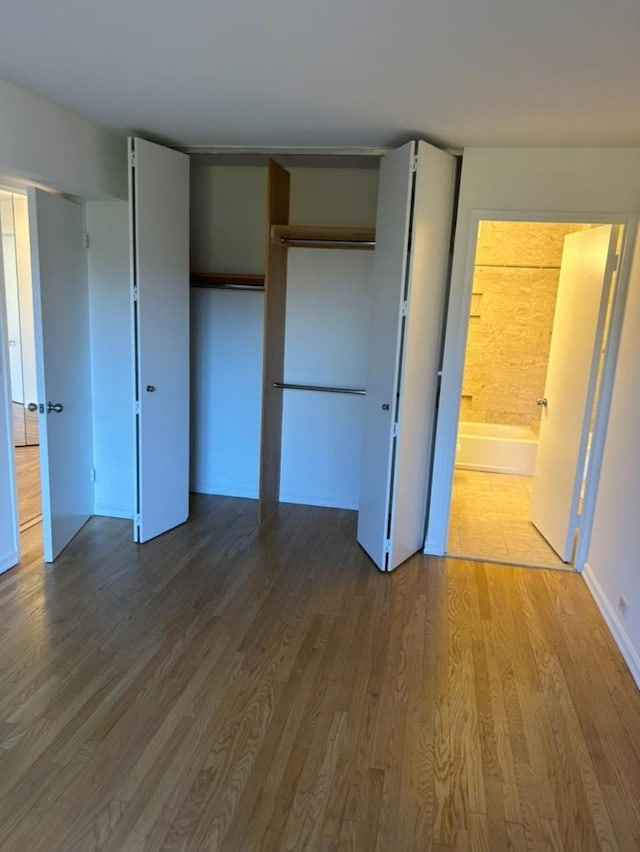 unfurnished bedroom with a closet, wood finished floors, and connected bathroom