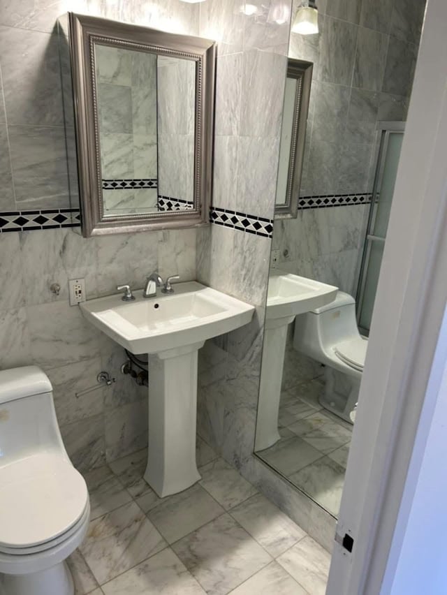 bathroom featuring marble finish floor, toilet, and tile walls