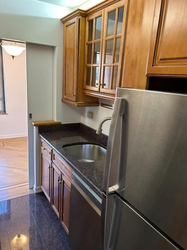kitchen with a sink, dishwasher, brown cabinetry, freestanding refrigerator, and baseboards