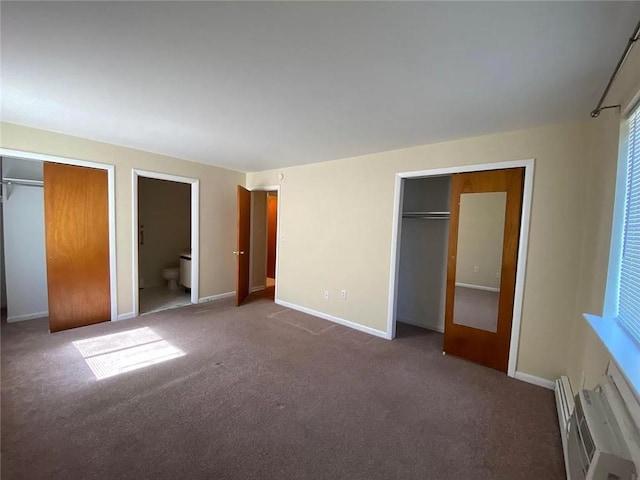 unfurnished bedroom featuring ensuite bathroom, dark carpet, a baseboard radiator, and two closets