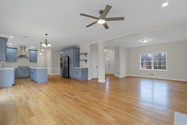 unfurnished living room with ceiling fan with notable chandelier, light wood-type flooring, and sink