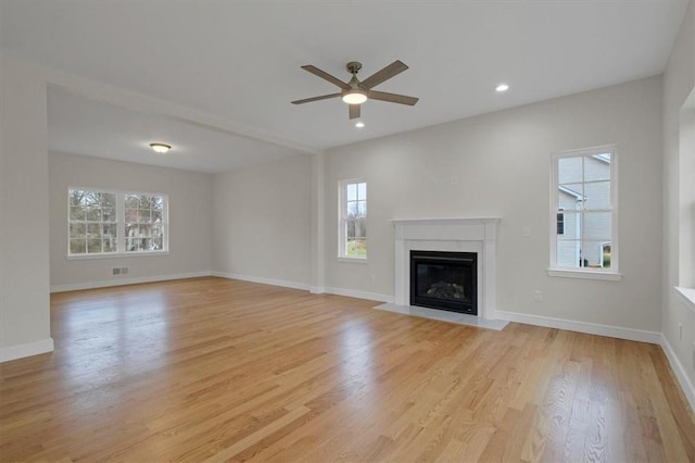 unfurnished living room featuring ceiling fan, a healthy amount of sunlight, a high end fireplace, and light hardwood / wood-style flooring