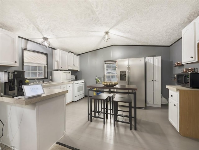 kitchen featuring a kitchen breakfast bar, white appliances, white cabinetry, and vaulted ceiling