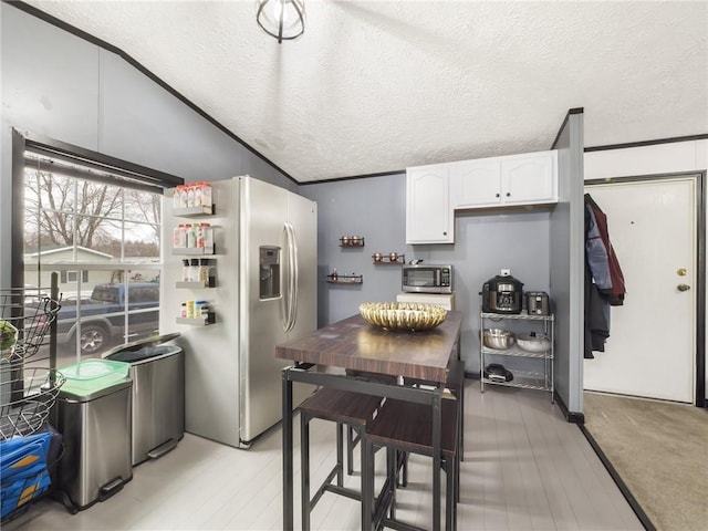 kitchen featuring a textured ceiling, stainless steel appliances, crown molding, white cabinetry, and lofted ceiling