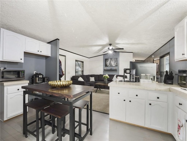 kitchen with a textured ceiling, white cabinetry, ceiling fan, and crown molding