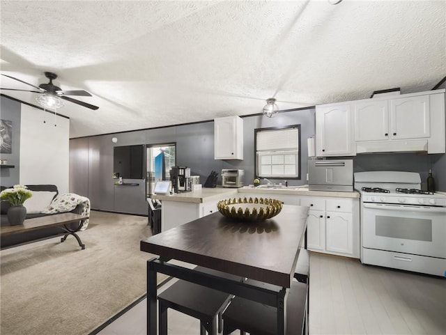 kitchen with a textured ceiling, light colored carpet, white cabinetry, and white gas range oven