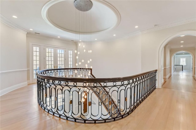 corridor featuring a raised ceiling, a healthy amount of sunlight, crown molding, and light hardwood / wood-style floors