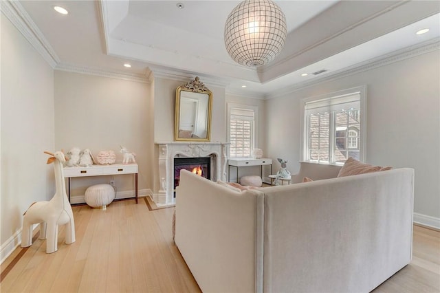 living room with a fireplace, light hardwood / wood-style floors, a raised ceiling, and ornamental molding