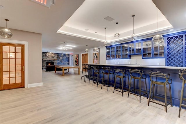 bar featuring a fireplace, decorative light fixtures, light hardwood / wood-style flooring, and a tray ceiling